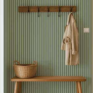 Pode incluir: Um corredor com um banco de madeira, um cesto de vime e um cabide com um casaco bege. A parede é decorada com riscas verticais verdes e brancas. A cena é bem iluminada e tem uma estética natural e terrosa.
