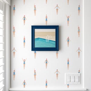 May include: White wall with a pattern of swimmers in blue swimsuits and pink swim caps. A framed painting of a pool with a blue frame hangs on the wall. The Wallpaper Tailor logo is in the bottom right corner.