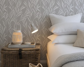 Puede incluir: Un dormitorio con un baúl de almacenamiento de mimbre trenzado sobre el que hay una linterna blanca y una pequeña lámpara de escritorio. Al lado hay una cama con almohadas blancas, un cojín de cuadros beige y una manta acolchada gris.