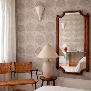 May include: A room interior featuring light beige wallpaper with a repeating shell and star pattern, a wooden bench with a woven seat, a table lamp with a textured base and conical shade, and a large rectangular mirror with a dark wood frame.