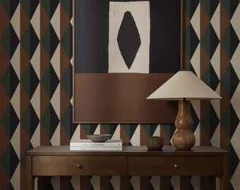 May include: A wooden console table with two drawers and a lower shelf, holding books and decorative items. A framed abstract artwork hangs above the table. A wooden lamp with a beige shade sits on the table. The background features a geometric diamond pattern wallpaper.