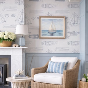 a cozy living room with a wicker chair, a white table, and a framed painting of a sailboat on the wall. The room has a nautical theme, with a blue and white color scheme and a wicker furniture style.