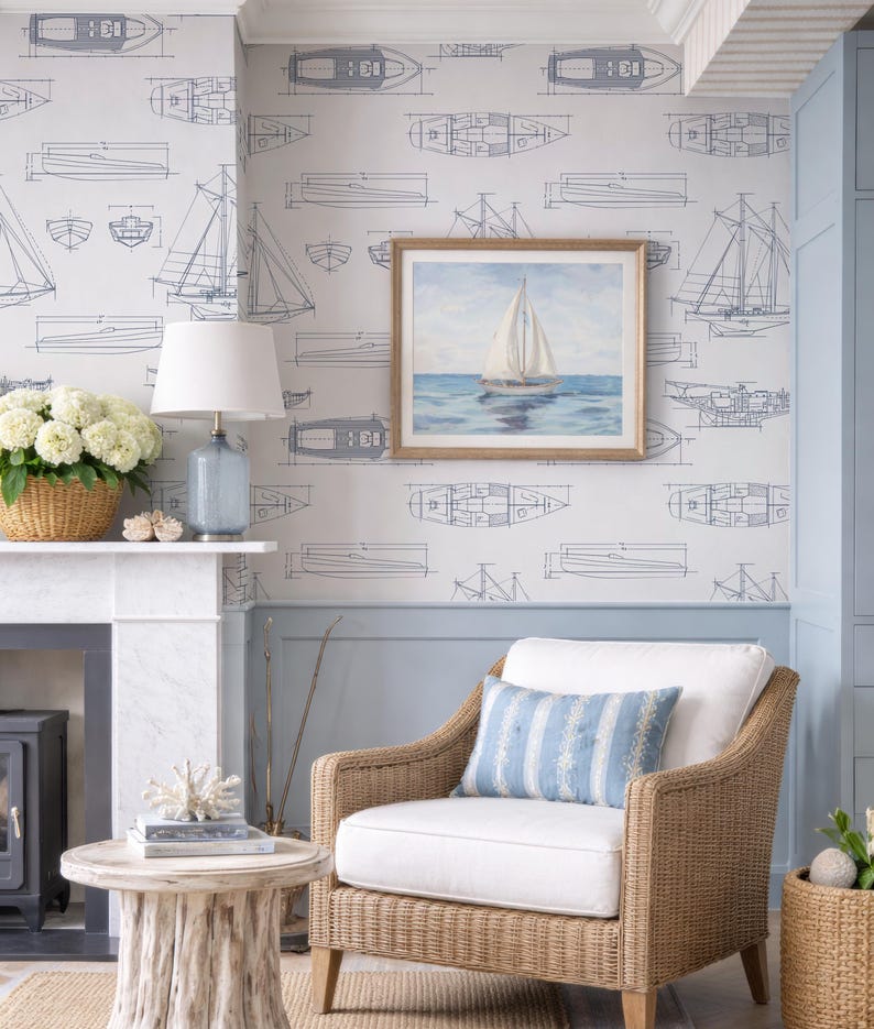 a cozy living room with a wicker chair, a white table, and a framed painting of a sailboat on the wall. The room has a nautical theme, with a blue and white color scheme and a wicker furniture style.