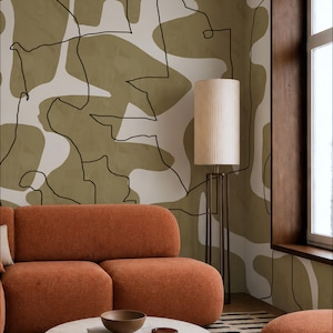Könnte beinhalten: Ein Innenraum mit einer Wand, die ein abstraktes Muster aus olivgrünen und cremeweißen organischen Formen zeigt, welche mit dünnen schwarzen Linien umrandet sind. Ein rostorangefarbenes Sofa steht vor der Wand neben einer hohen Stehlampe.