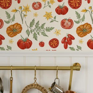 May include: A kitchen scene featuring a wallpaper with a repeating pattern of red and orange tomatoes, yellow flowers, and green leaves. Below, a brass rod holds various kitchen utensils, including a woven trivet, a small metal pitcher, and a copper pot.