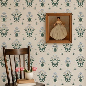 Pode incluir: Um quarto com papel de parede floral em creme, verde e azul. Uma cadeira de madeira suporta livros e um vaso com tulipas cor-de-rosa. Um retrato emoldurado adorna a parede, adicionando um toque artístico clássico.