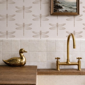 a bathroom with a dragonfly wallpaper, a gold-colored sink faucet, a gold-colored duck figurine, and a framed painting of a landscape on the wall.