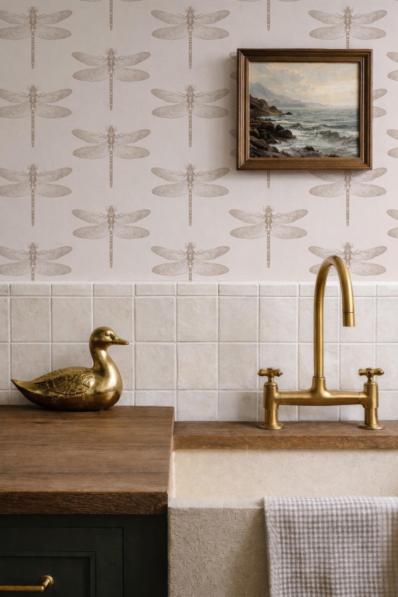 a bathroom with a dragonfly wallpaper, a gold-colored sink faucet, a gold-colored duck figurine, and a framed painting of a landscape on the wall.
