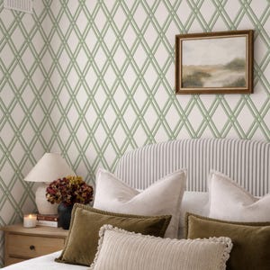 Könnte beinhalten: Schlafzimmer-Interieur mit einem Bett mit gestreiftem Kopfteil und Kissen in Weiß, Beige und Olivgrün. Die Wand ist mit einer Tapete mit Gittermuster in Weiß und Hellgrün und einem gerahmten Landschaftsbild geschmückt.