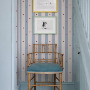 Könnte beinhalten: Ein Vintage-Stuhl aus Bambus mit einem Sitz aus blaugrünem Samt steht vor einer gestreiften Tapete mit gerahmter Kunst. Die Tapete hat blaue und beige vertikale Streifen mit roten Punkten. Zwei gerahmte Bilder hängen über dem Stuhl.