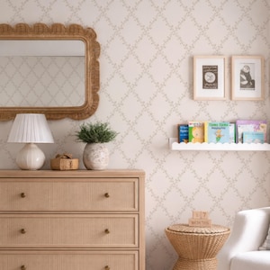 Puede incluir: Una cómoda de madera clara con tres cajones, una lámpara blanca y un espejo tejido. La habitación tiene una combinación de colores neutros con papel pintado estampado y una pequeña mesa auxiliar. Se ven libros y fotos enmarcadas.