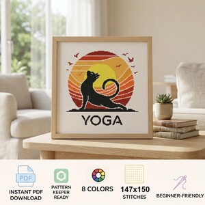 May include: A cross-stitch pattern featuring a black cat in a yoga pose against a circular sunset background of yellow, orange, and red stripes. The word YOGA is printed in black capital letters below the cat. The design includes small bird silhouettes.