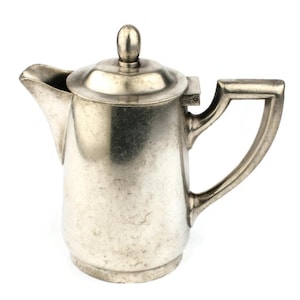 Könnte beinhalten: Eine silberne Milchkännchen mit abgerundetem Körper und einem Griff. Die Milchkännchen hat eine glatte, polierte Oberfläche.