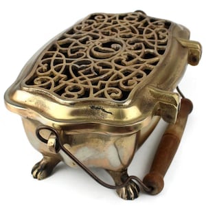 Puede incluir: Un quemador de incienso de metal dorado con un diseño decorativo calado y un asa de madera. El quemador tiene cuatro patas y está diseñado para contener conos o varillas de incienso.