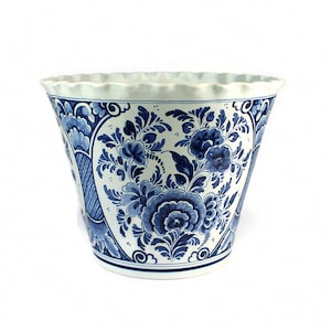 Puede incluir: Una maceta de cerámica blanca con un diseño floral azul y blanco. La maceta tiene un borde festoneado y una base acampanada.