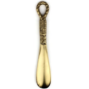 May include: A gold metal shoehorn with a rope-like handle.
