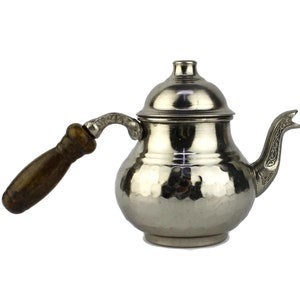 May include: A silver teapot with a hammered finish and a wooden handle. The teapot has a decorative spout and a lid.