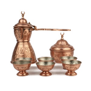 Puede incluir: Un juego de café turco tradicional con una cafetera de cobre, un azucarero y cuatro tazas pequeñas. El juego está decorado con intrincados patrones florales y geométricos.