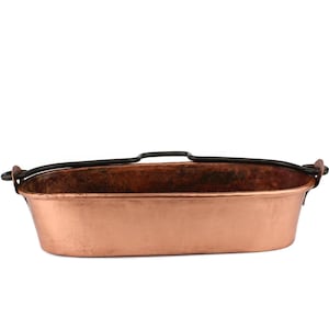 Op de afbeelding: Een ovale koperen braadpan met zwarte ijzeren handvatten. De pan heeft een gehamerde afwerking en is perfect voor het koken van verschillende gerechten.