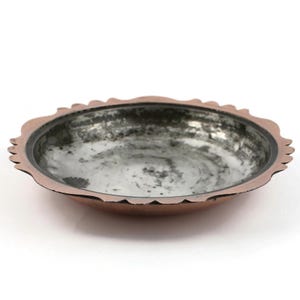 May include: A copper-colored bowl with a scalloped rim. The interior has a mottled, silvery appearance. The bowl's rim is a darker shade of copper, and the overall design is simple and elegant. The bowl is likely handmade.