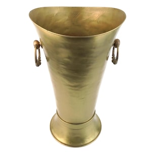 Puede incluir: Una taza de cerámica blanca con asa negra y el texto "But First, Coffee" en negrita negra. La taza está llena de un líquido oscuro, probablemente café, y se encuentra sobre una superficie clara.