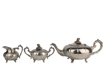 May include: A silver teapot, creamer, and sugar bowl set with ornate details and a bulbous shape.