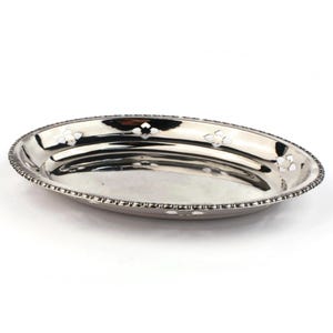 Peut inclure: Un plat de service ovale argenté avec un bord perlé et des motifs floraux blancs. Le plat a une surface très polie et réfléchissante. Le plat de service mesure environ 25 cm de long et est idéal pour présenter des aliments.