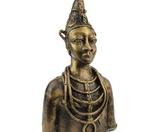 May include: A bronze-colored bust of a person with a detailed headdress and layered necklace. The sculpture has a textured surface and a serene facial expression. The bust is a decorative art piece.