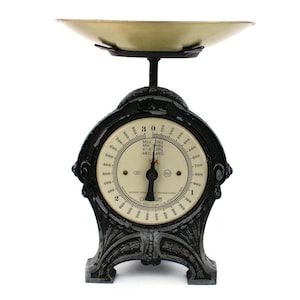 May include: An antique black and gold kitchen scale with a circular dial and a brass-coloured weighing pan. The dial displays numbers up to 900, with a maximum weight of 3 kg. The scale has an ornate, decorative base.