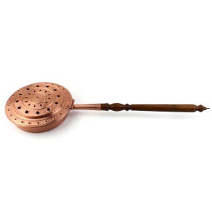 May include: A copper stove top kettle with a wooden handle. The kettle has a round, perforated base and a long, slender handle.
