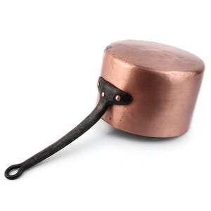 Peut inclure: Une casserole en cuivre avec une poignée en métal foncé. Le pot a un corps arrondi et une longue poignée incurvée fixée avec des rivets. La surface en cuivre a une teinte brun-rougeâtre chaude.