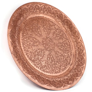Peut inclure: Un plateau ovale en cuivre avec des motifs floraux et géométriques en relief. Le plateau présente un bord festonné et un motif central en forme d'étoile. Le métal a une teinte brun-rougeâtre chaude, et les détails sont finement travaillés.
