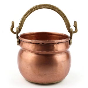 May include: A small, copper-colored cauldron with a rounded body and a brass handle. The handle is arched and attached to the cauldron with decorative hooks. The cauldron has a polished finish and is likely used for decorative purposes.