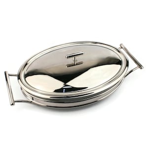 Puede incluir: Una fuente ovalada y brillante con tapa y asas. La fuente de acero inoxidable tiene una superficie reflectante y un pequeño asa en la tapa. Las asas son curvas y se extienden desde los lados de la fuente.