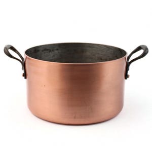 Puede incluir: Una olla de cocina de cobre con dos asas curvas. La olla tiene un exterior marrón rojizo brillante y un interior más oscuro. Las asas son de un metal más oscuro y la olla es redonda con una amplia abertura.
