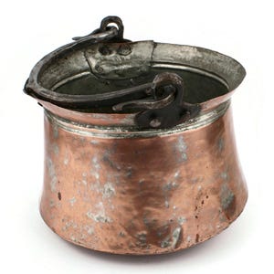 Könnte beinhalten: Ein antiker Kupfertopf mit gehämmerter Oberfläche und einem Scharniergriff aus Eisen. Der Topf hat eine abgenutzte Patina und wird wahrscheinlich zum Kochen verwendet.