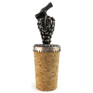 May include: A wine bottle stopper featuring a silver-coloured grape cluster design. The stopper has a cork base and a decorative metal top. The grape cluster is detailed and adds a touch of elegance.