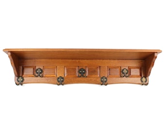 May include: A wooden coat rack for wall mounting, featuring a shelf and six decorative metal hooks. The rack is crafted from light brown wood, with a rectangular shelf above the hooks. The hooks are dark metal with ornate detailing. A practical storage solution.