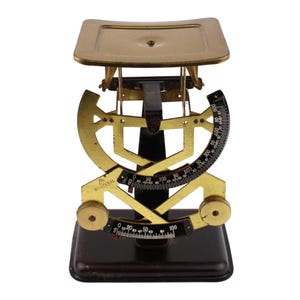 Könnte beinhalten: Eine mechanische Waage im Vintage-Stil mit dunkelbraunem Sockel und goldfarbenem Metallrahmen. Die Waage verfügt über eine obere Wiegeplattform, ein gebogenes schwarzes Zifferblatt mit weißen Markierungen von 0 bis 500 und eine untere Skala mit der Aufschrift Bilateral.