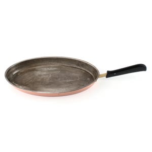 May include: An oval-shaped copper frying pan with a dark, worn interior surface and a long, black handle attached by a brass-colored metal neck. The exterior of the pan features a polished copper finish, while the handle is smooth and curved.