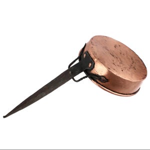 May include: A copper saucepan with a long, dark metal handle. The pan has a rounded base and a slightly flared rim. The handle is attached with rivets and has a twisted design near the pan. The copper has a warm, reddish-brown colour.