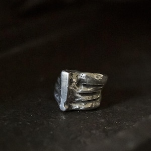 Puede incluir: Un anillo de plata con un diseño texturizado y abstracto. El anillo está hecho de metal y tiene un aspecto áspero y orgánico.
