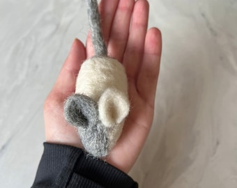 May include: A small, hand-crafted felt mouse toy with a white body and grey ears and tail.