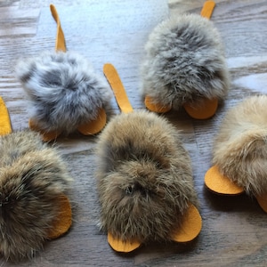 May include: Five handmade cat toys shaped like mice with long tails. The mice are made of brown and gray fur with yellow felt ears and tails.