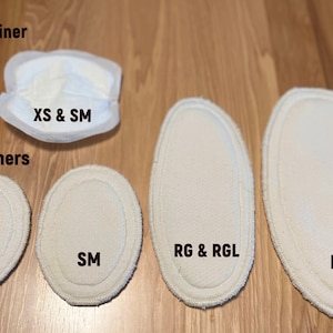 May include: An assortment of white reusable and disposable liners for personal care. The image shows various sizes, including XS, SM, RG & RGL, and LG & XL, along with a disposable liner labeled XS & SM. The text "Reusable liners" and "Disposable liner" are also visible.
