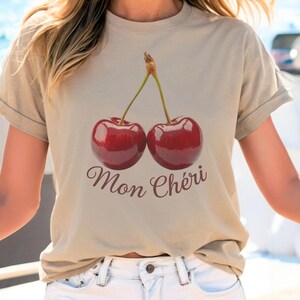May include: A beige t-shirt with a graphic of two red cherries and the text "Mon Ch&eacute;ri" in brown.