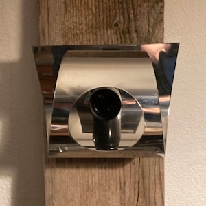 Può includere: Un'applique da parete argentata con un'apertura circolare al centro. L'applique è montata su una superficie in legno.