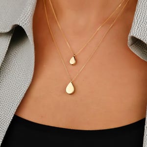 Op de afbeelding: Een gelaagde gouden ketting met drie druppelvormige hangers. De hangers zijn van verschillende grootte en zijn allemaal van hetzelfde gouden materiaal.