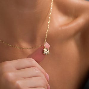 May include: A delicate gold-colored necklace featuring a paw print pendant. The pendant is small and detailed, with rounded paw pads. The chain is thin and elegant, creating a minimalist and charming accessory.