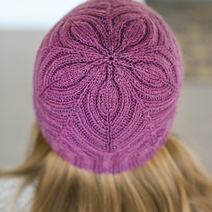 May include: A purple knitted hat with a floral pattern. The hat is made with a soft yarn and has a comfortable fit.